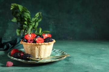 Sweet tartlet with different fresh berries and mint on green background