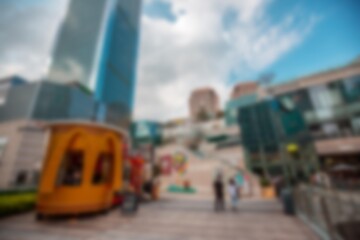 A blurred image of a city street with a tall building, small shops, and a walkway.