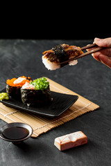 Hand Holding Chopsticks with Sushi on Black Background