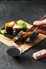 Hand Holding Sushi with Fresh Ingredients and Soy Sauce on Table