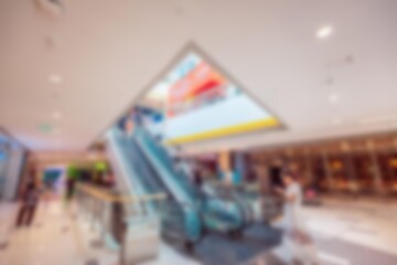 A blurred image of an escalator in a large shopping mall with people walking.