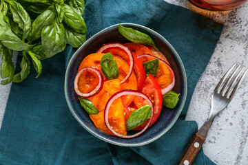 Bowl of fresh tomato salad with red onion and basil leaves on grey background