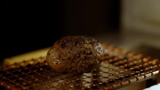 Close-up of a juicy Japanese hamburg steak sizzling and releasing flavorful smoke. The rich browning and steam create an aroma and visual appeal. Perfect for culinary videos, restaurant promotions.