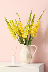 Vase with beautiful yellow gladiolus flowers on chest of drawers near pink wall