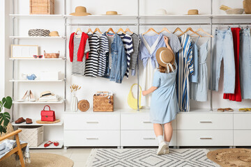 Young woman with hanging clothes in wardrobe, back view