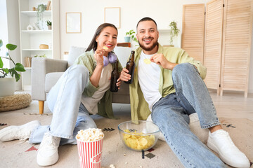 Young couple with beer and chips watching sport game at home