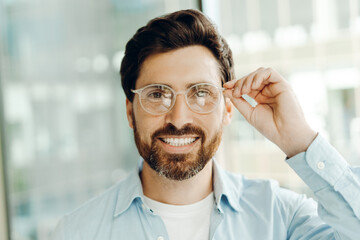 Obraz premium Smiling businessman adjusting eyeglasses in office setting