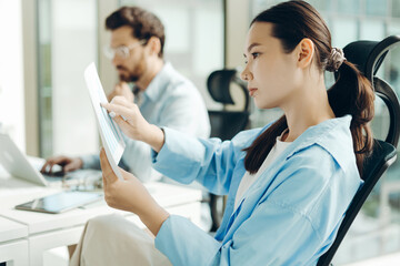 Businesswoman analyzing charts in modern office with colleague working in background