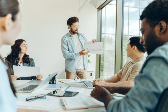 Diverse group of team, marketing manager showing growth chart to colleagues during office meeting