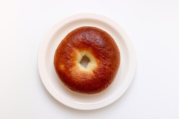 A delicious plain bagel. A well-baked, brown loaf. A single bagel placed on a round plate.