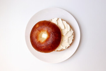 A delicious plain bagel topped with cream cheese. A single bagel on a round plate.