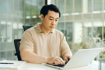 Fototapeta premium Focused asian businessman working on laptop in modern office