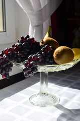 glass vase with fruits on table by window on sunny day