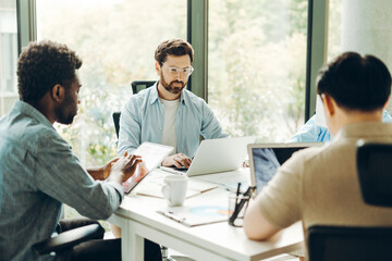 Diverse group of team collaborating on project in modern office using laptops and digital tablet