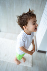 Fototapeta premium Cute child joyfully playing indoors. A young boy with tousled hair is smiling and enjoying himself while playing inside a bright, minimalistic room.