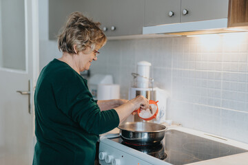 An older woman is seen cooking in a modern kitchen, involved in her meal preparation, highlighting everyday life and culinary skills.