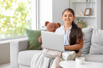 Fototapeta premium Little girl using laptop on sofa at home