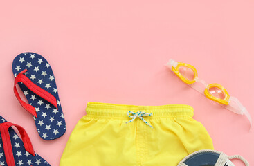 Children's swim shorts with goggles and flip-flops on pink background