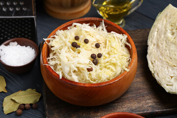 Bowl with tasty sauerkraut, peppercorns and bay leaves on black wooden background, closeup