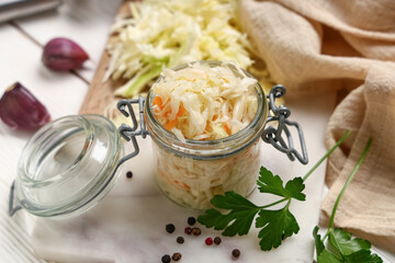 Jar with tasty sauerkraut and different ingredients on white wooden background, closeup