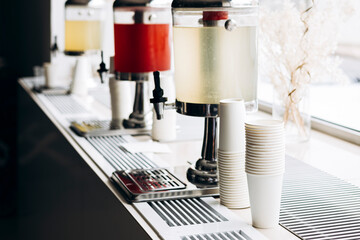 Colorful cold drink dispensers with paper cups in interior setting.