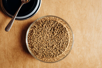 Glass jar with buckwheat tea granules on light wooden table, close up.