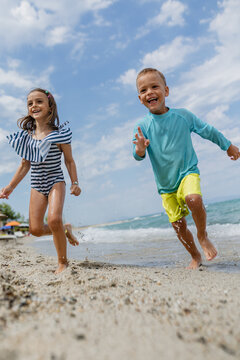 Children play joyfully on the beach while splashing in the water under a partly cloudy sky during a summer afternoon