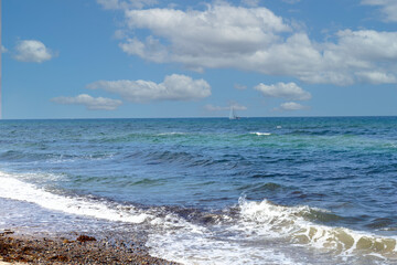 Waves move on blue sea under clear sky, yacht far away.
