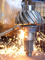 Sparks fly from a welding torch as it works on a pinion gear differential and shaft, a powerful...