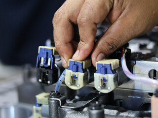 A technician's hands connect wires and solenoid on a automatic transmission control valve, illustrating precision and detail in mechanical assembly.