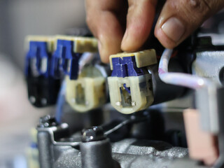 A technician's hands connect wires and solenoid on a automatic transmission control valve, illustrating precision and detail in mechanical assembly.