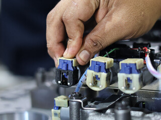 A technician's hands connect wires and solenoid on a automatic transmission control valve, illustrating precision and detail in mechanical assembly.