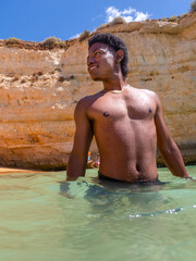 Handsome young tourist traveler African American man vacations swims in ocean at Senhora da Rocha beach in the Algarve coast of Portugal beautiful cliffs nature landscape background