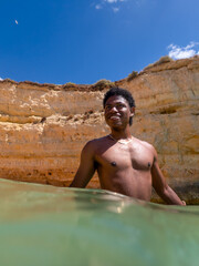 Handsome young tourist traveler African American man vacations swims in ocean at Senhora da Rocha beach in the Algarve coast of Portugal beautiful cliffs nature landscape background