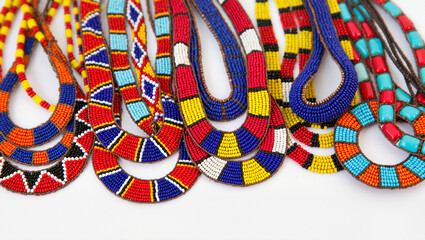 A close-up view of a collection of vibrant Maasai beaded jewelry. The necklaces and bracelets feature a mix of bold geometric patterns in red, blue, yellow, and white.