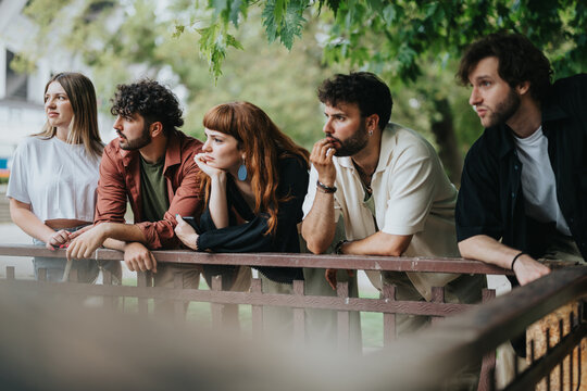 Five young adults enjoying time outdoors, leaning on a wooden railing in a lush park. Capturing candid moments of friendship and leisure within a vibrant natural environment. - Powered by Adobe