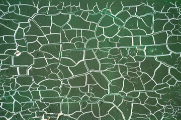 Bizarre white cracks in peeling dark green paint. Weathered surface of a painted electrical box. High-contrast macro shot. Vintage or lost place background with small island-like structures.