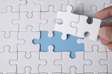 Obraz premium Close-up of a hand placing the final puzzle piece into a blue gap, symbolizing problem-solving, finding the missing piece, completion, decision-making, and achieving a solution.