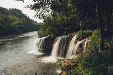 Sai Yok Yai waterfall flowing into the river Kwai surrounded by lush vegetation, creating a serene natural landscape in Kanchanaburi, Thailand