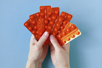 Tablets in orange blister pack in hands of Caucasian woman. Blue background. Top view.