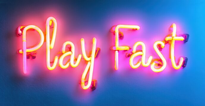 Bright neon sign displays words Play Fast. Vivid pink glows against blue wall. Modern aesthetic, simple message.