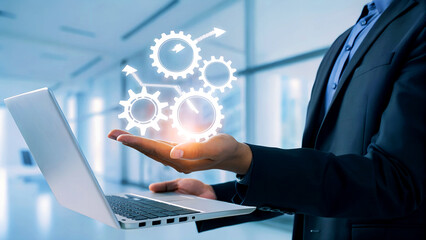 Dynamic businessman presents innovative workflow with glowing gears and laptop, symbolizing progress and efficiency in modern business.