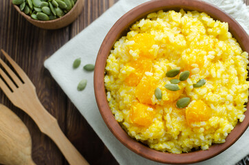 Pumpkin risotto in a ceramic bowl on a napkin with seeds on a brown wooden table. Italian food concept. Rustic style. Autumn food. Selective focus. Horizontal orientation. Copy space. Top view