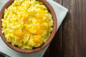 Pumpkin risotto in a ceramic bowl on a napkin on a brown wooden table. Italian food concept. Rustic style. Autumn food. Selective focus. Horizontal orientation. Copy space. Top view