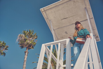 Female lifeguard standing in a white lifeguard tower, ensuring beach safety on a sunny summer day
