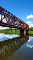 Obraz premium Rusty red train bridge over a calm river