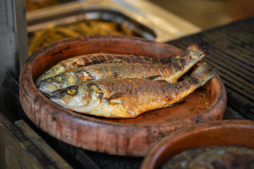 Three whole grilled fish with crispy skin and golden color served on rustic clay plate. Concept of grilled fish, rustic food, traditional beer festival