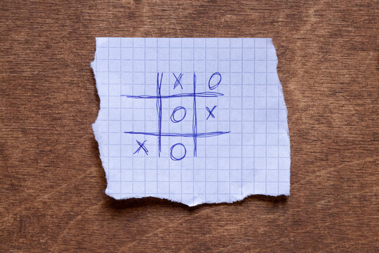 Tic Tac Toe drawn on squared paper lying on wooden surface, game