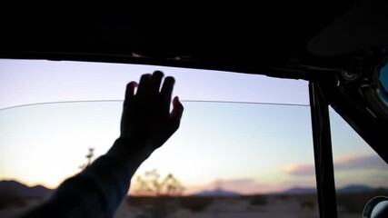 A Hand Reaches Out to a Desert Sunset Through a Car Window, a Journey's Silhouette