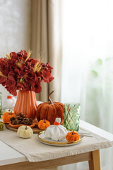 Thanksgiving table setting with decorative pumpkins, candles and string lights on white wooden table